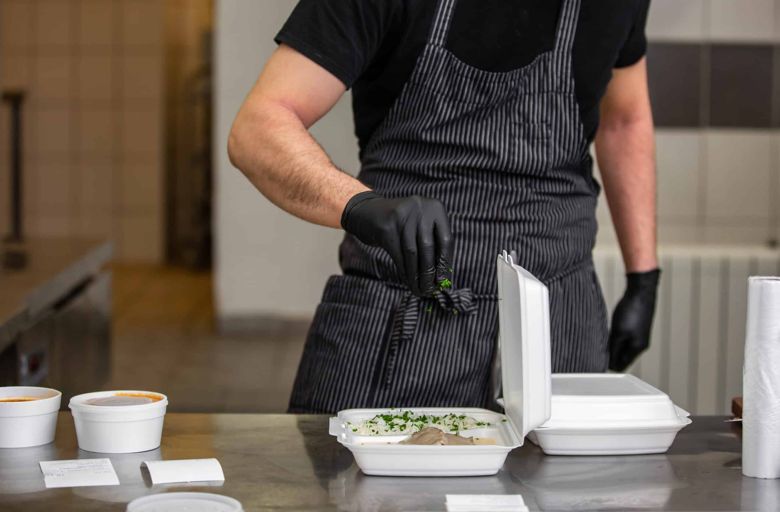 Chef preparing dish to a box in the restaurant for food delivery service to home, online ordering